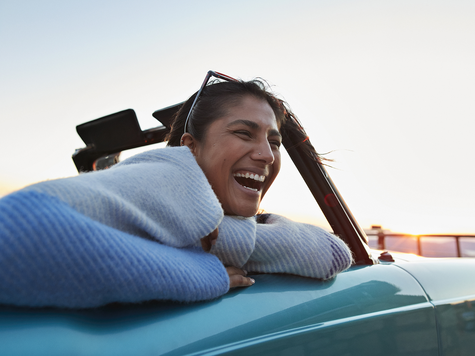 Cheerful young woman in convertible car enjoying road trip during sunset