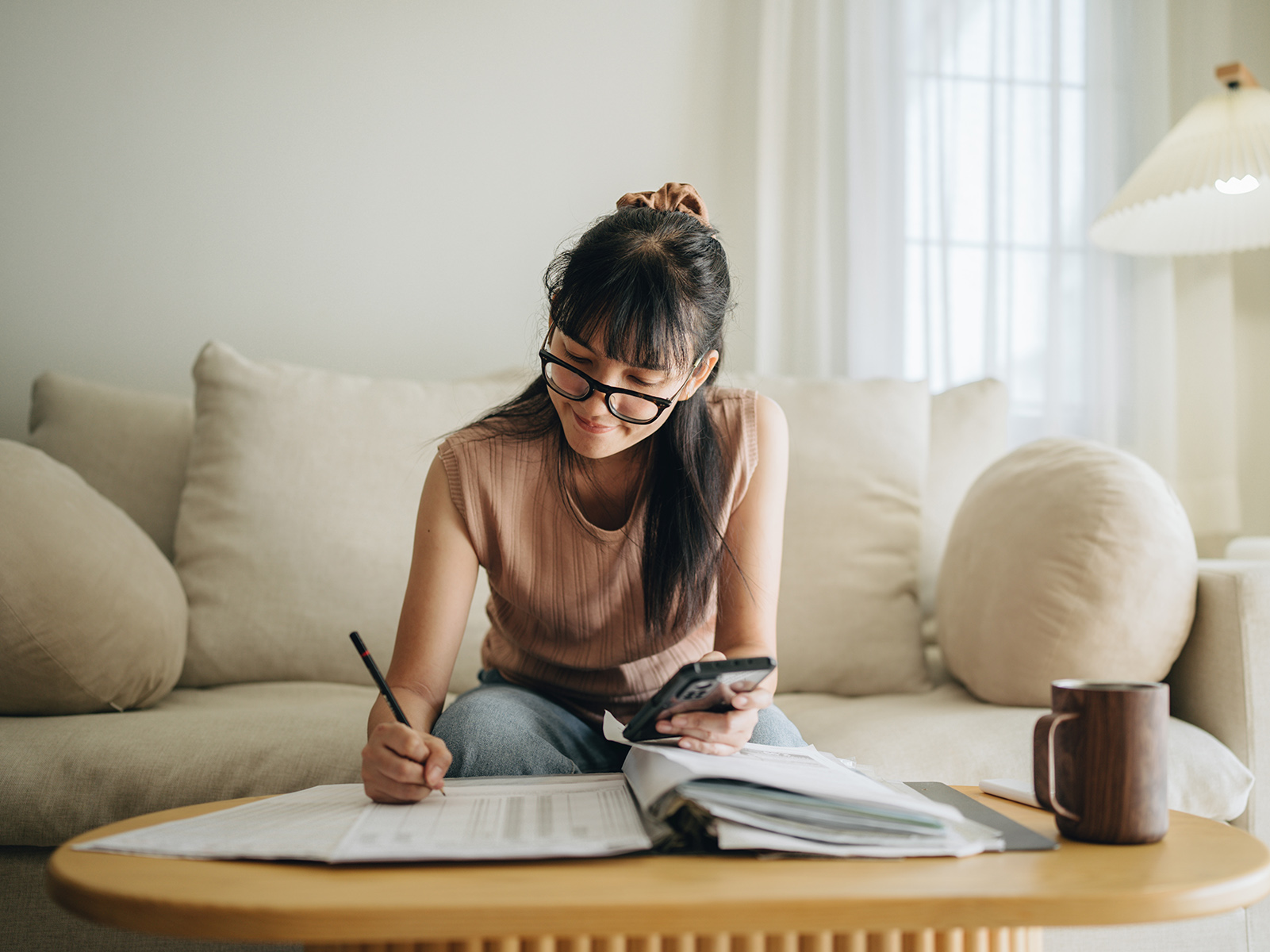 Young woman sitting at a coffee table, writing in a ledger.