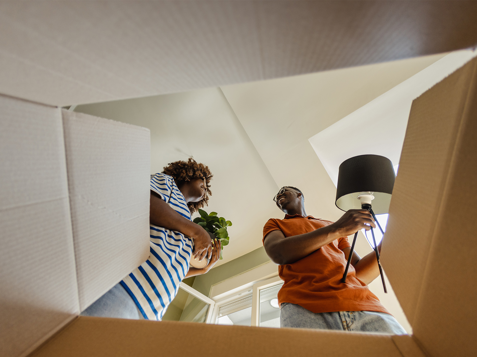 A young couple smiling while unpacking furniture from moving boxes.