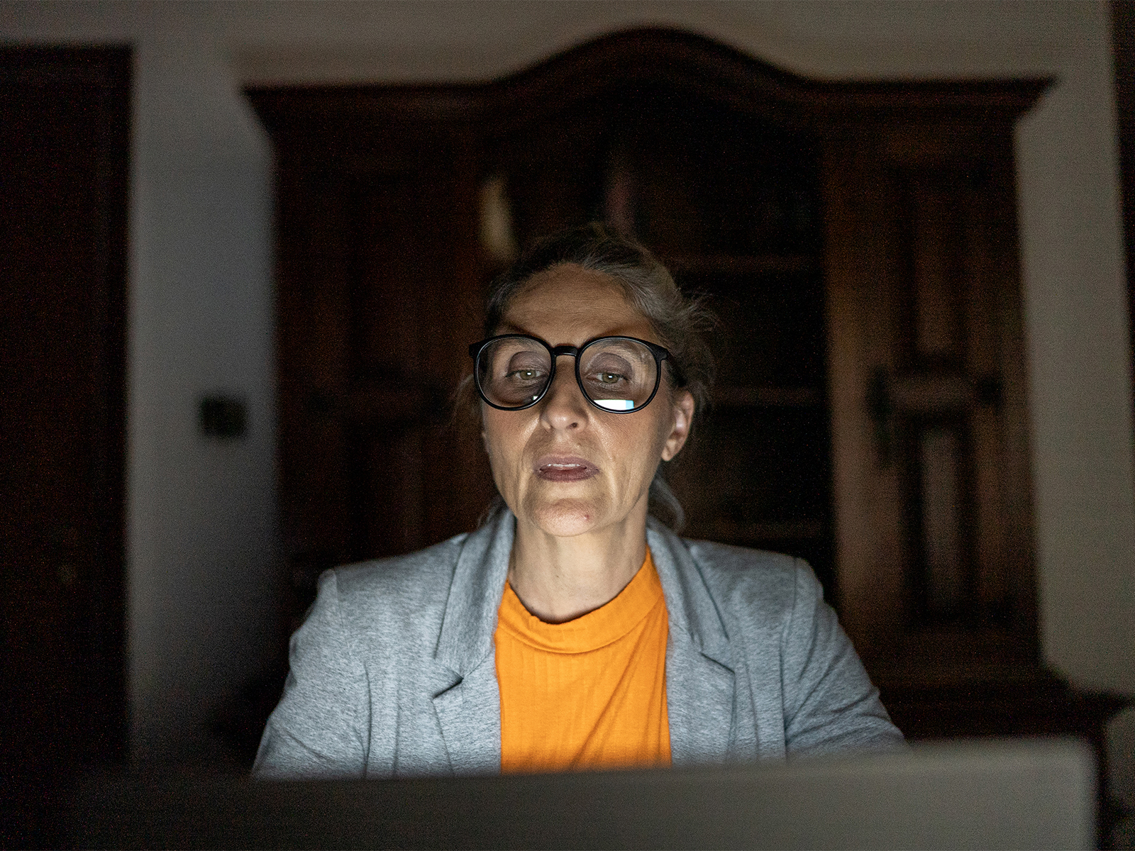 An older woman sitting in front of her computer, the screen illuminating the worried look on her face.