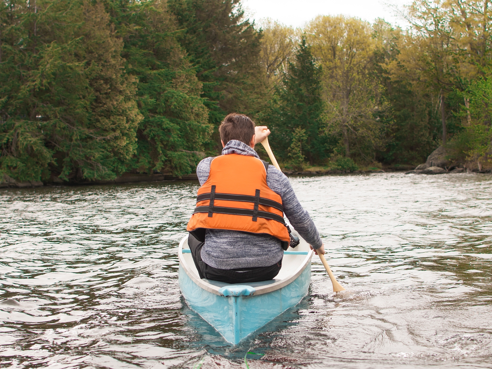 A man canoeing in a river wearing an orange life jacket.