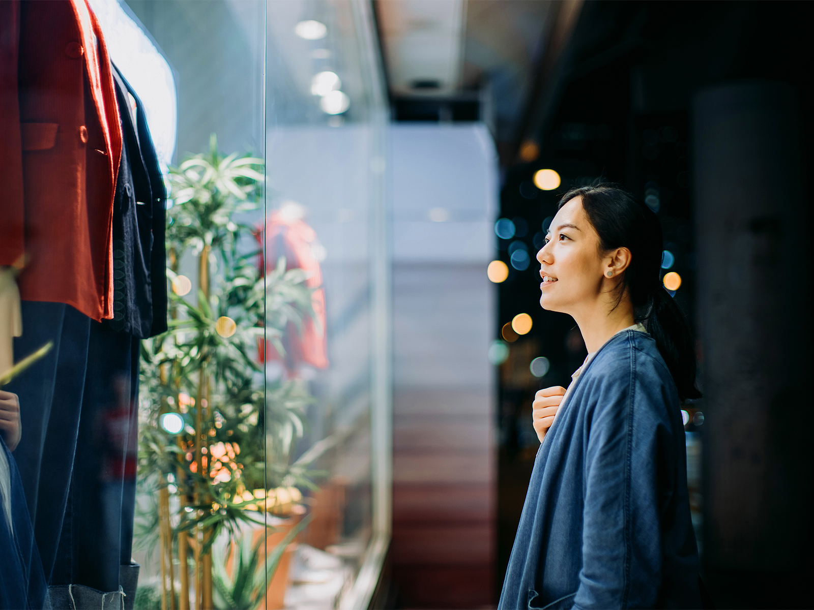 A woman looking at clothing on mannequins in a storefront window display.