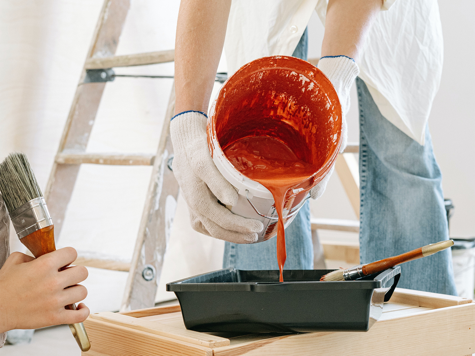 A person pouring a bucket of orange paint into a pain tray.