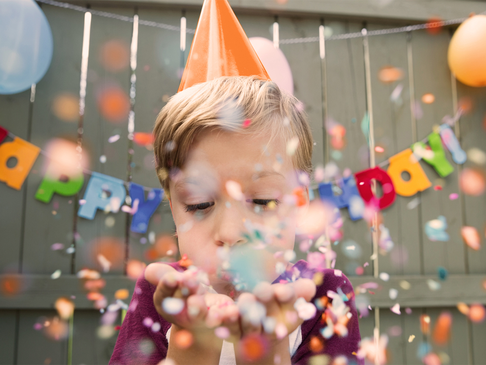 A young boy wearing a birthday hat, blowing confetti.