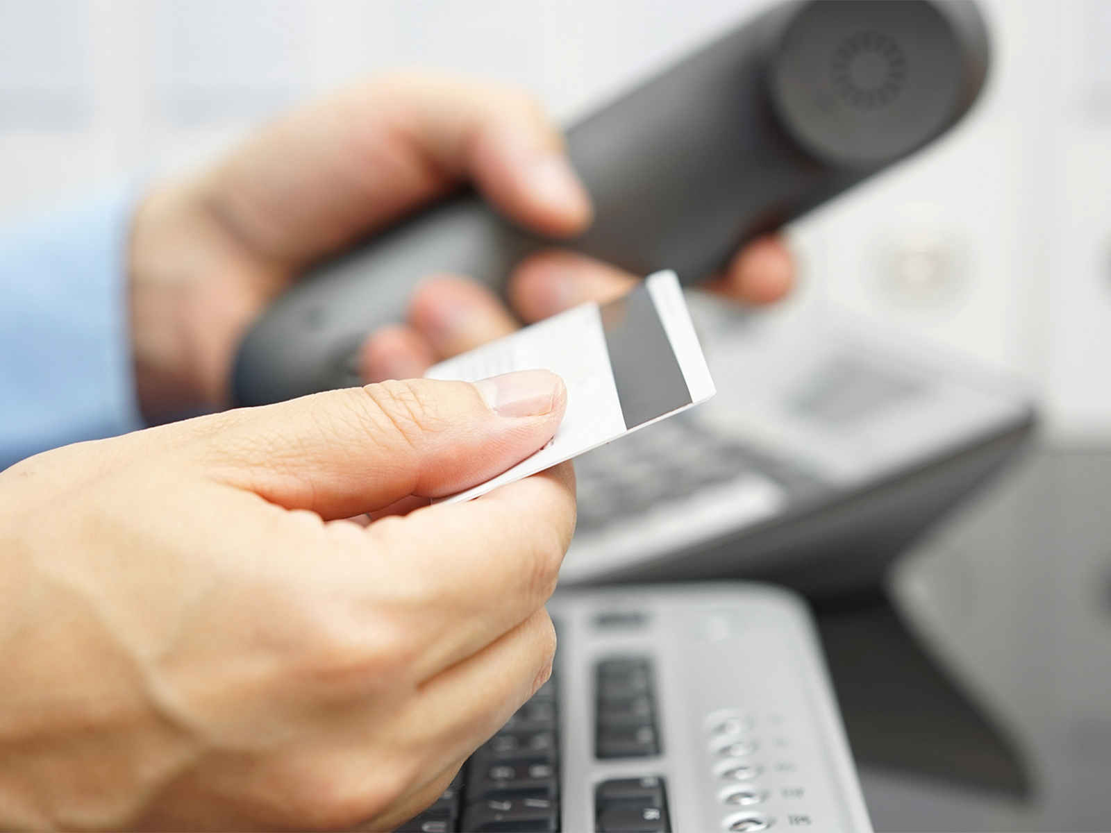 A person looking at the numbers on the back of his credit card while dialing on a telephone.