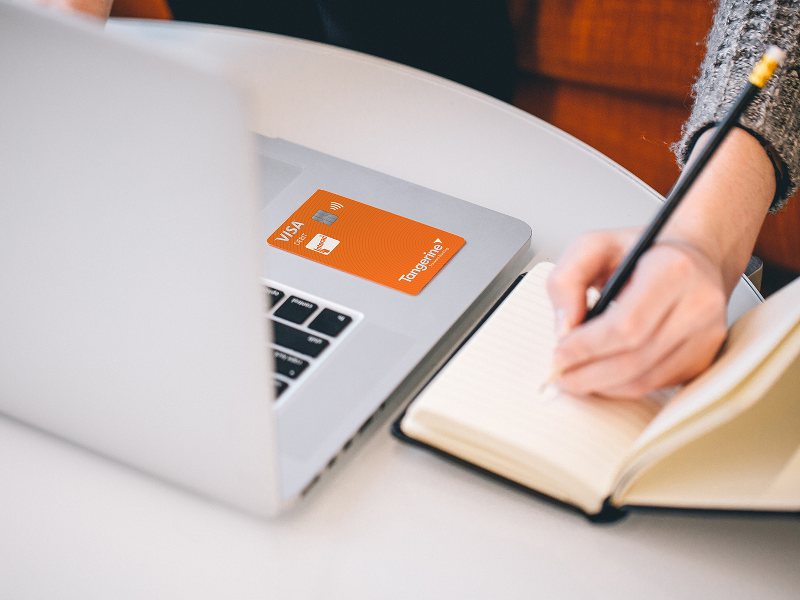 An open laptop on a table with a Tangerine debit card placed on it.