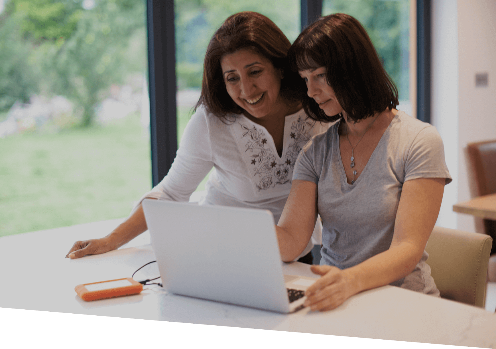 A lady showing an older lady the content on a PC screen.