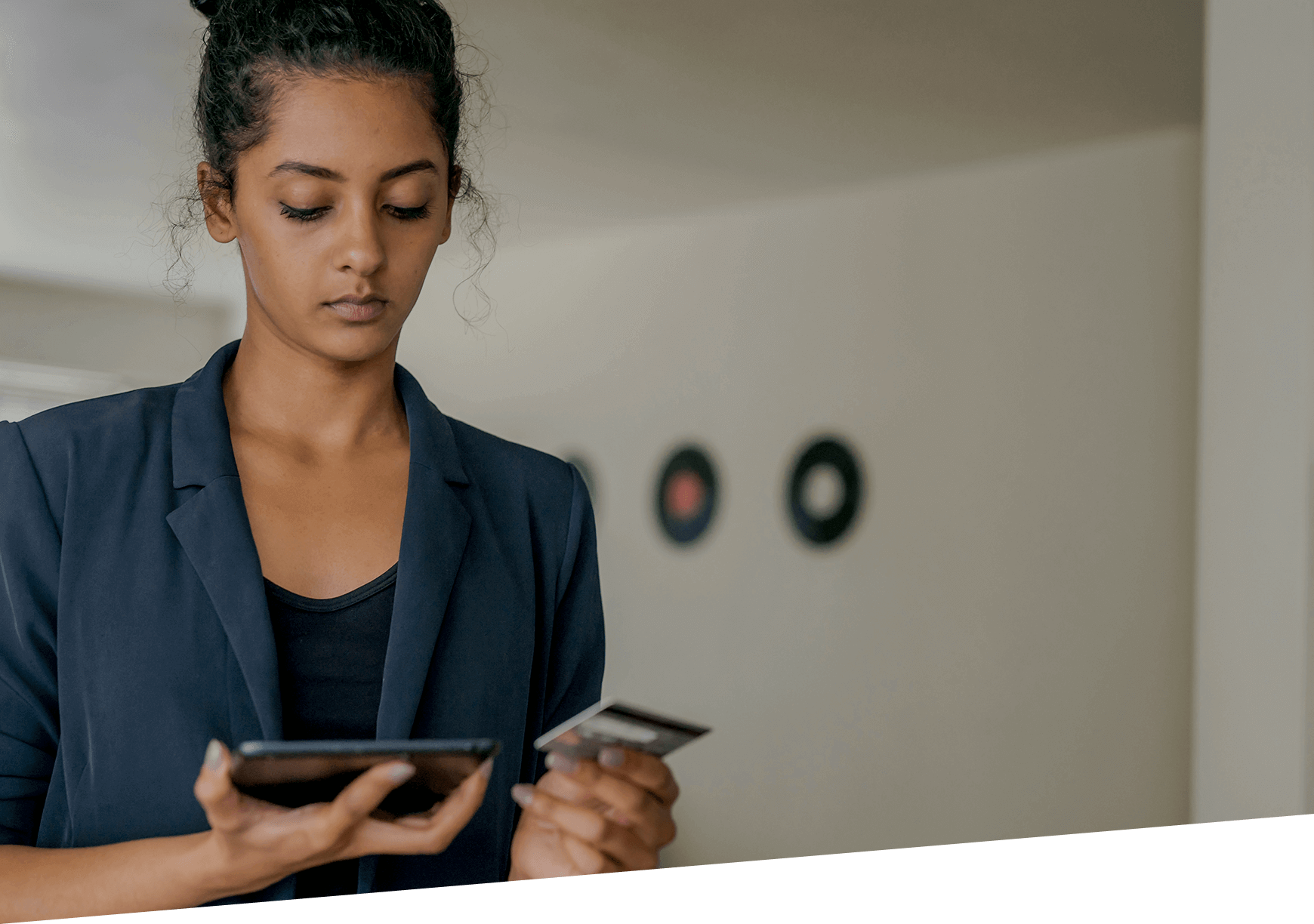 Une femme regardant une table1e qu’elle ent d’une main tout en tenant une carte de paiementdans l’autre main.