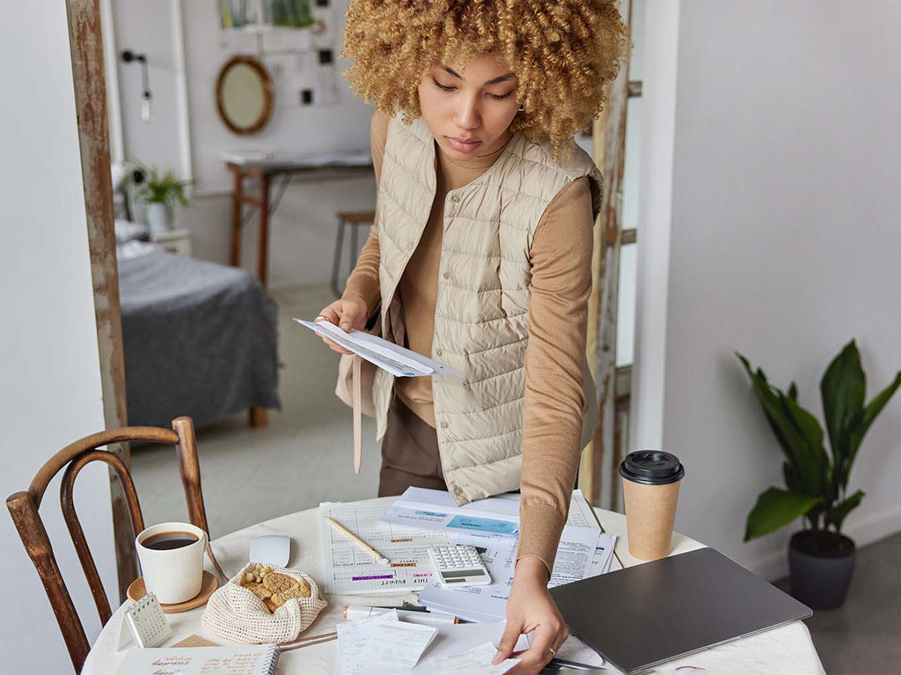 A worrying young woman looking through a pile of bills and receipts on her kitchen table.