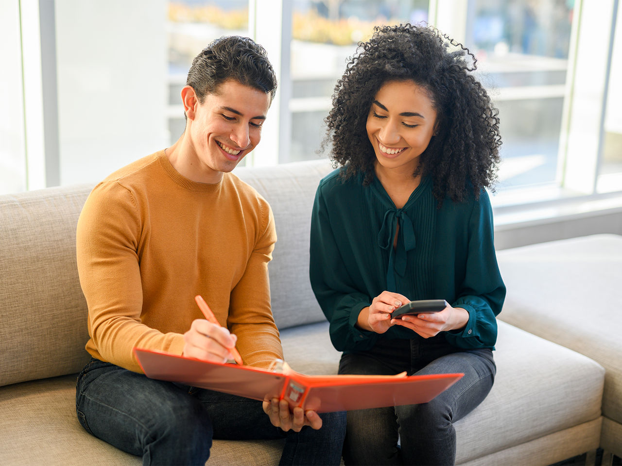 Two young adults, a man and a woman, sitting together and looking at an orange binder.