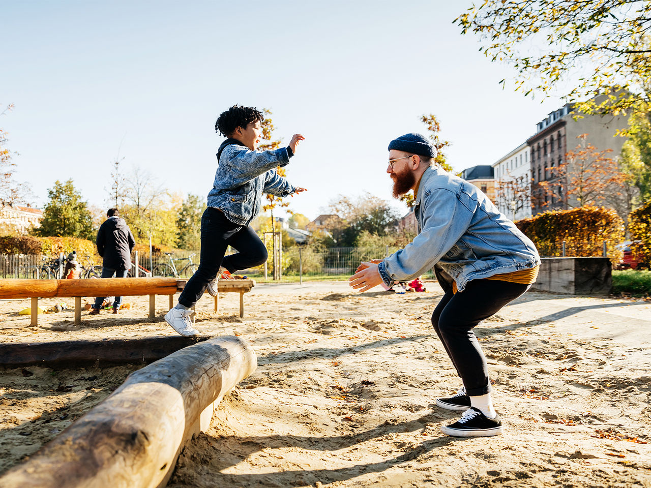 A child jumping off an outdoor wooden play structure into his father's arms.