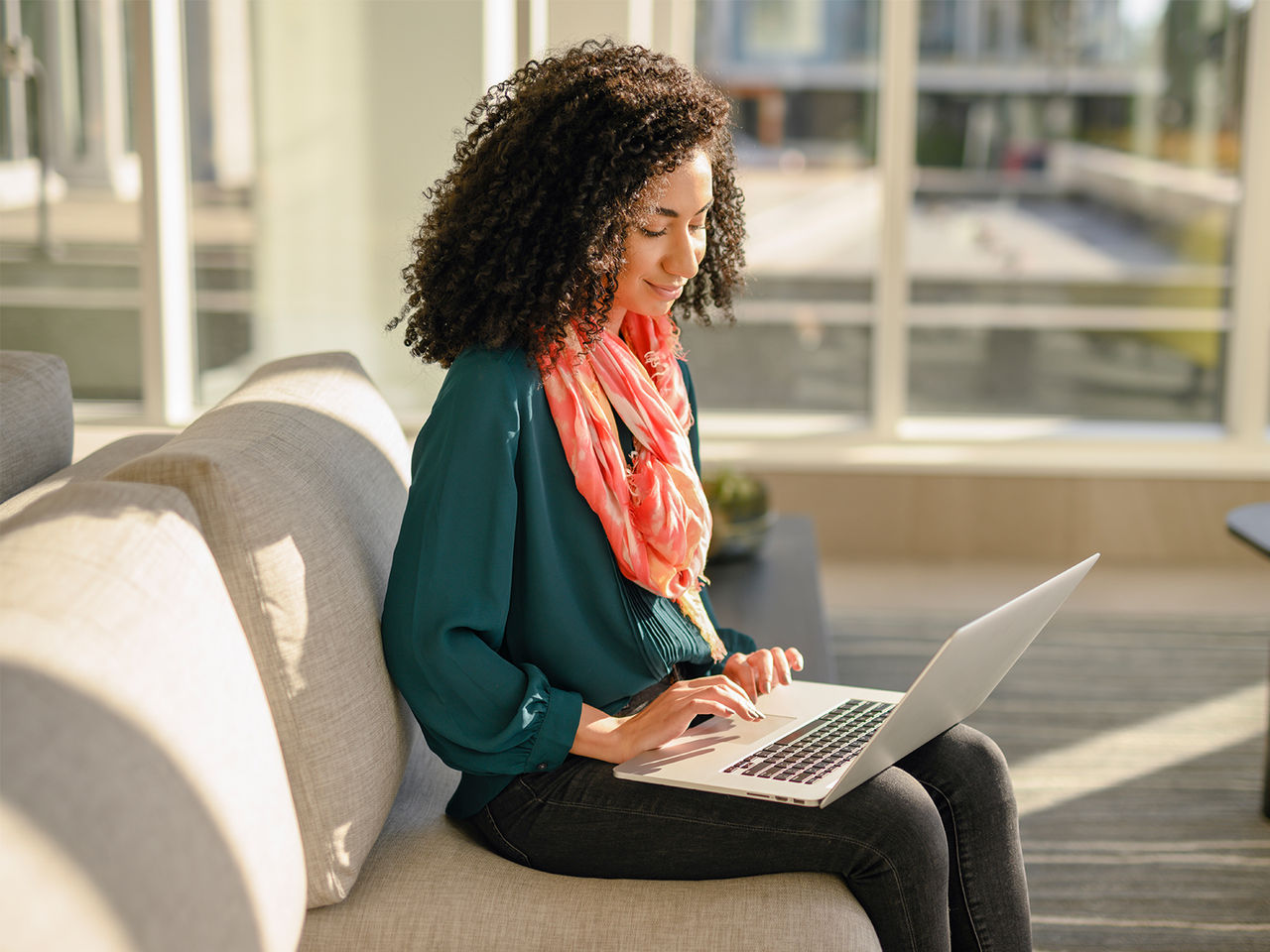 A smiling woman sitting on a couch and using a laptop.