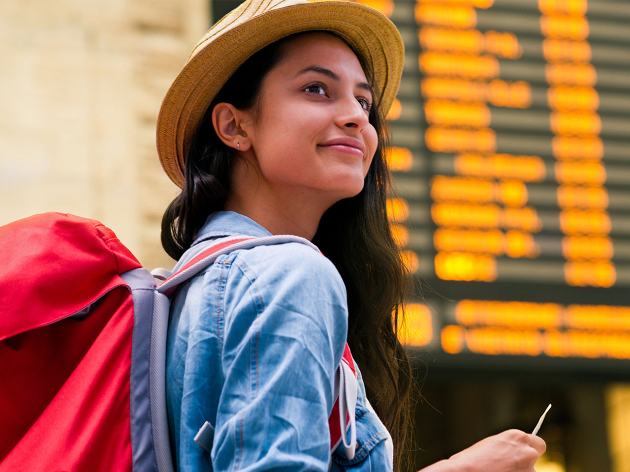 A young woman with a large backpack waiting at a train station, ticket in hand.