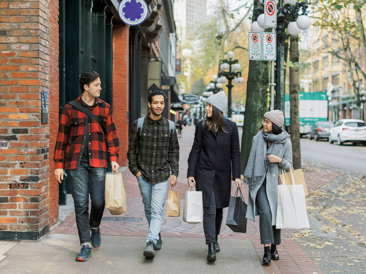 A group of four young adults, walking on a sidewalk, while carrying shopping bags in their hands.