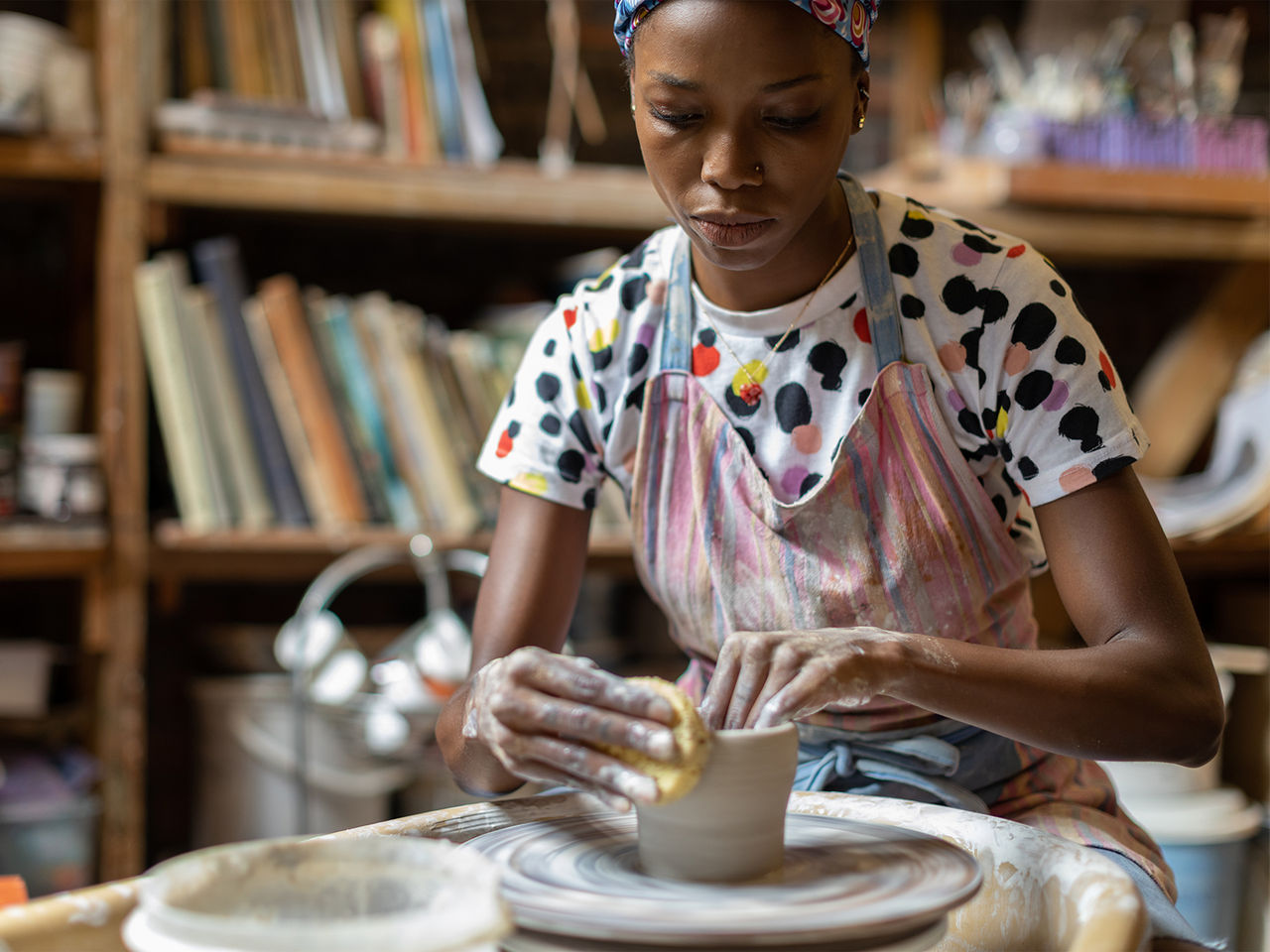 A woman sitting in front of a pottery wheel, building a piece out of clay. 