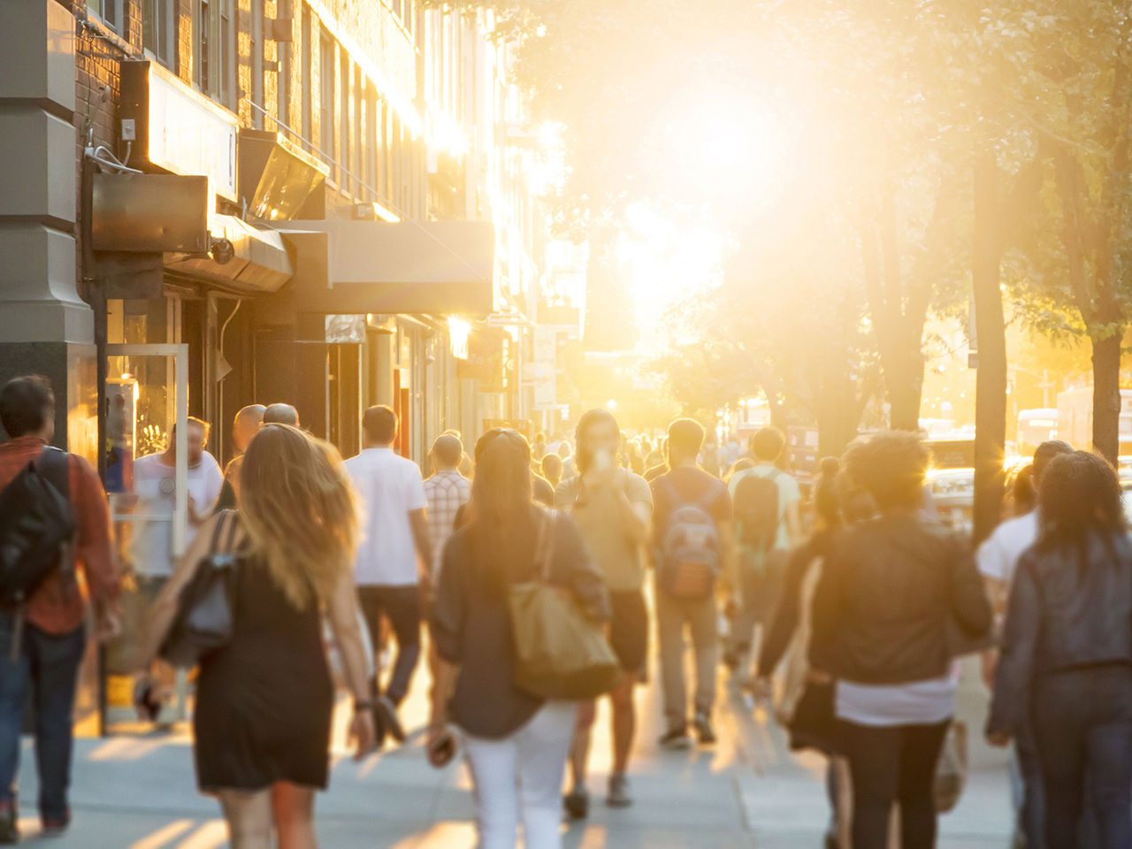 Crowd of anonymous men and women walking down an urban sidewalk with bright glowing sunlight in the background on a busy street in downtown Manhattan, New York City 